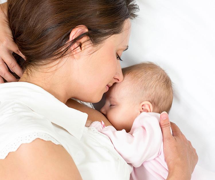 Baby breastfeeding as mom holds baby closely