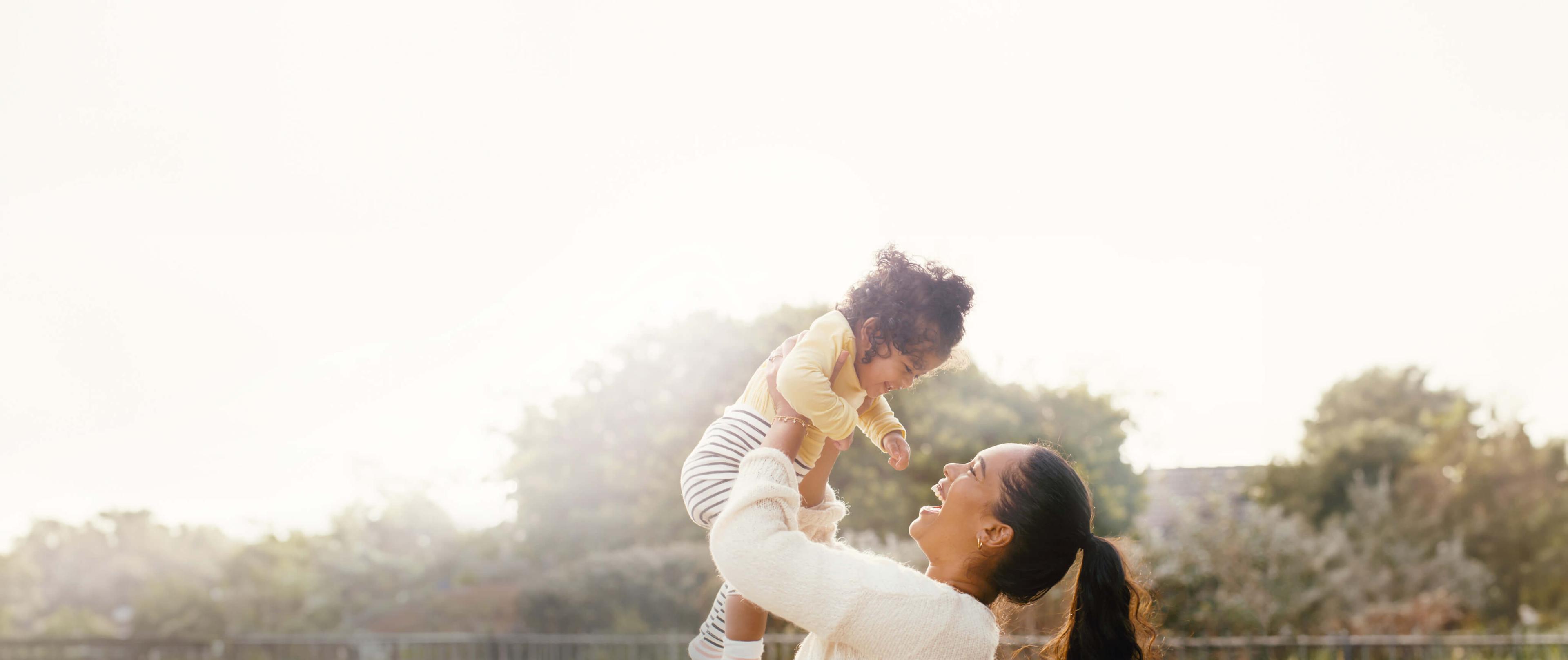 Parent joyfully lifting baby in sunlit outdoor setting
