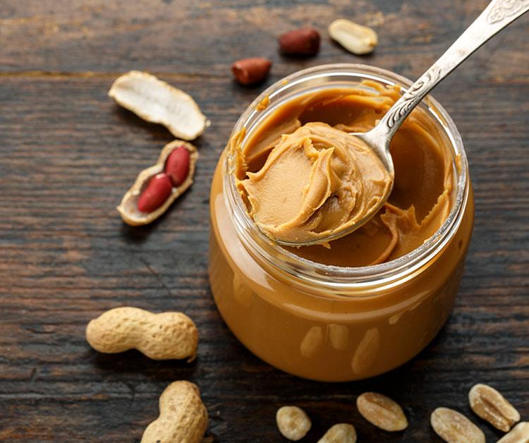 A jar of peanut butter and scattered peanuts
